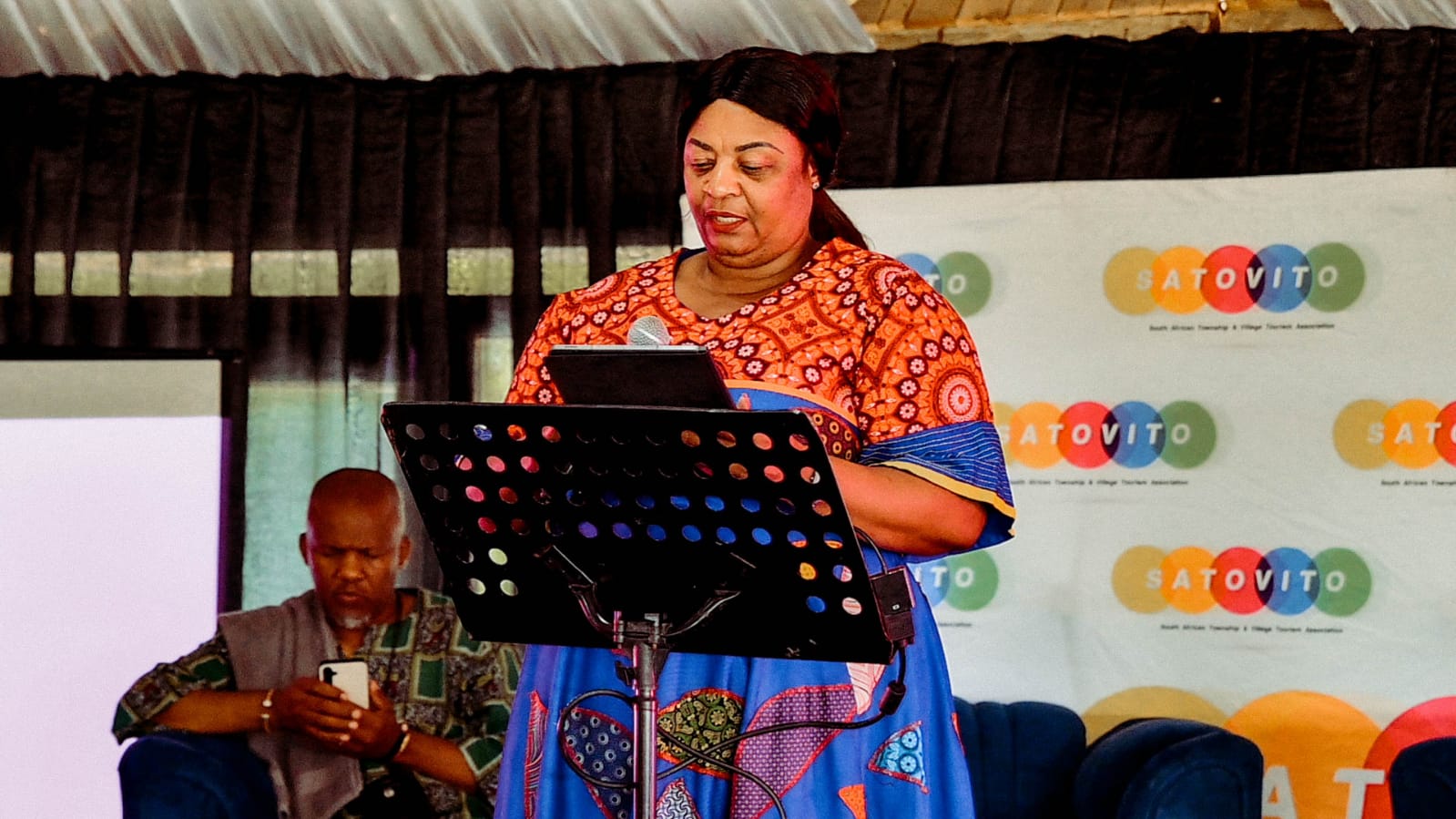 A speaker at a lectern in front of SATOVITO branding